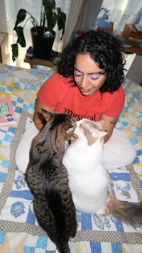 a woman is petting two cats on a bed