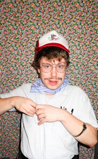 a man with a mustache and glasses posing in front of a floral background