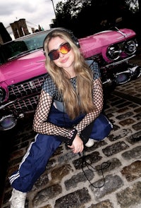 a woman is crouching down next to a pink car