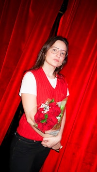 a woman holding a bouquet of roses in front of a red curtain