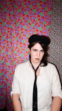 a woman wearing a hat and tie in front of a colorful wall